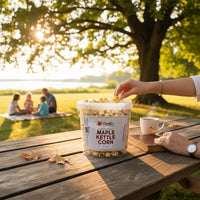 Doodle's Sugarbush, LLC - 100% Pure Michigan Maple Syrup kettle corn in a clear tub on a wooden table at a park.
